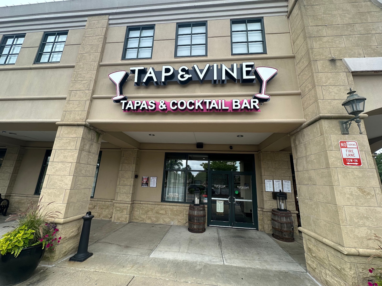 PHOTO-2025-07-01-10-22-36 Front view of Tap & Vine Tapas & Cocktail Bar with wine bottle display tree and covered patio entrance in Ballantyne, Charlotte, NC.
